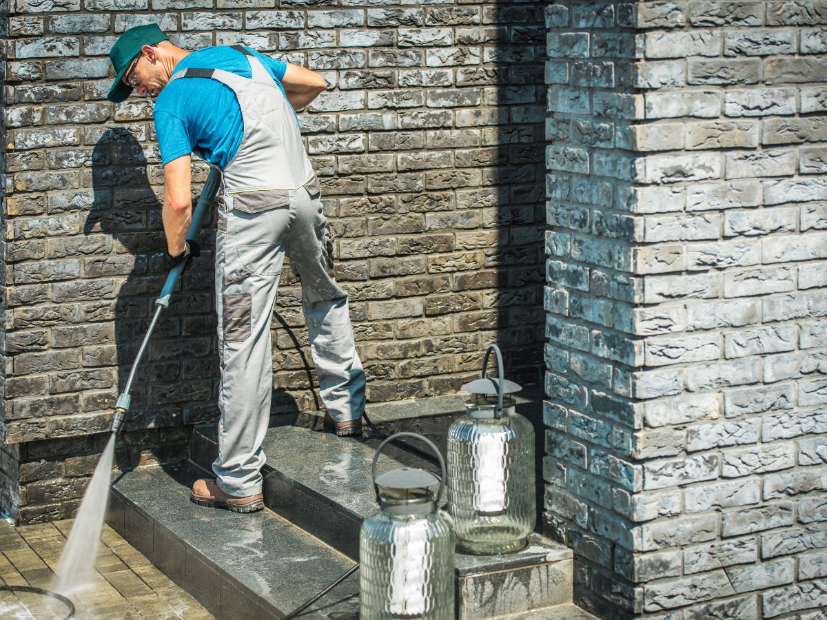 Worker pressure washing brick wall and steps outside a house.