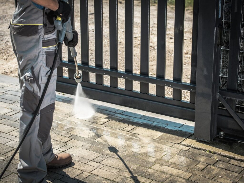 Concrete Cleaning Services in Bridgewater, MA: Driveways, Patios & Pool Decks 2 Cleaning paved driveway near metal gate with pressure washer.