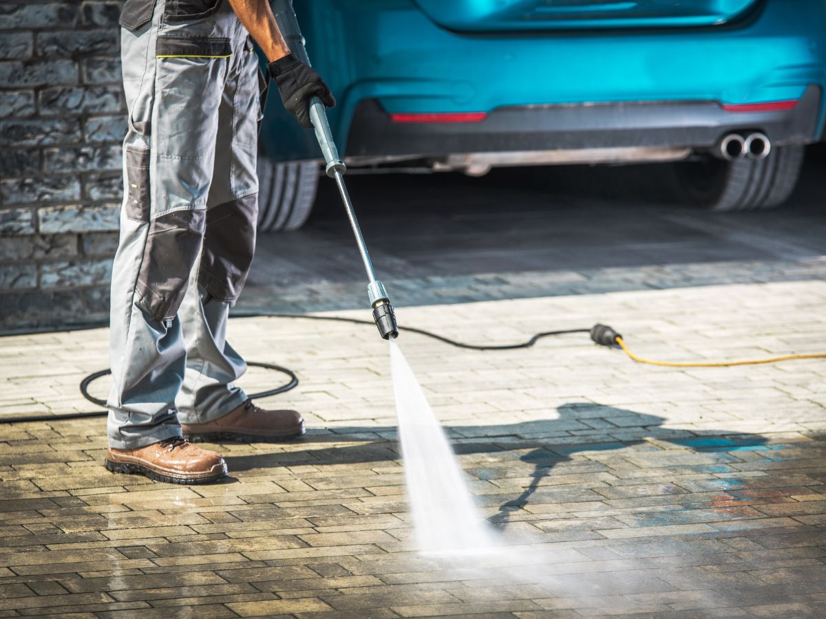 Close-up of pressure washing driveway beside parked car.