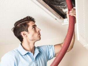 Technician inspecting and cleaning air duct with hose.