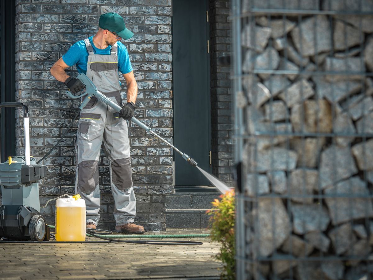 Worker pressure washing front steps with cleaning solution.