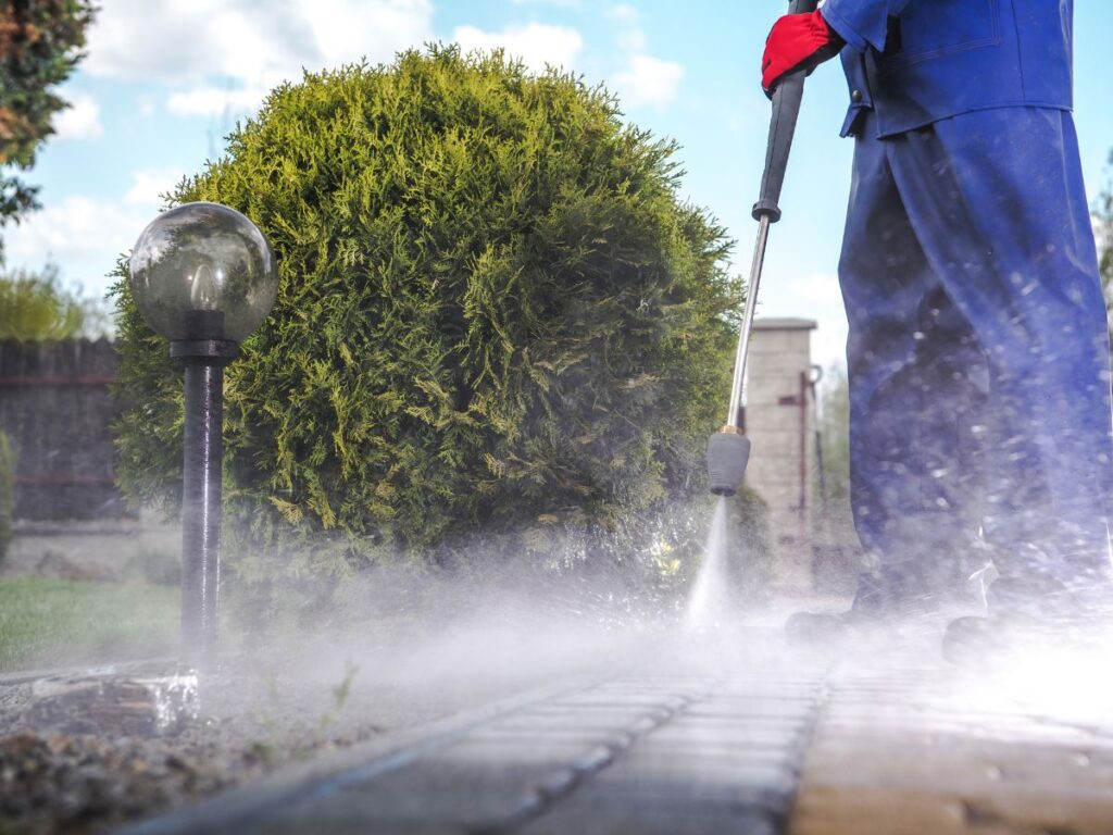Professional Pressure Washing in Bridgewater, MA: What Makes South Shore Soft Wash Different 1 Worker in protective gear pressure washing walkway beside trimmed hedge.